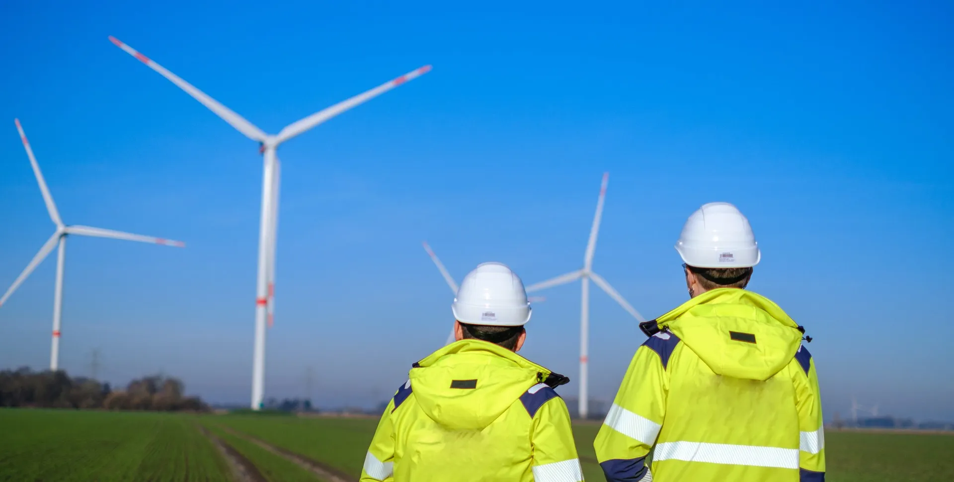 Zwei Personen in Schutzausrüstung vor Windkraftanlagen